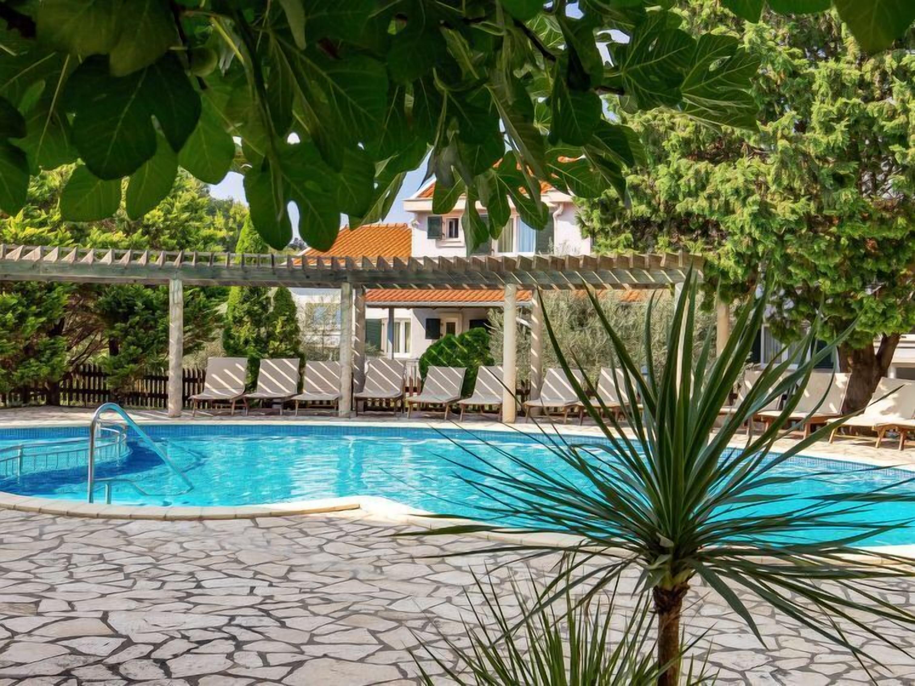 A swimming pool with a stone-tiled deck, lounge chairs, and a pergola structure.