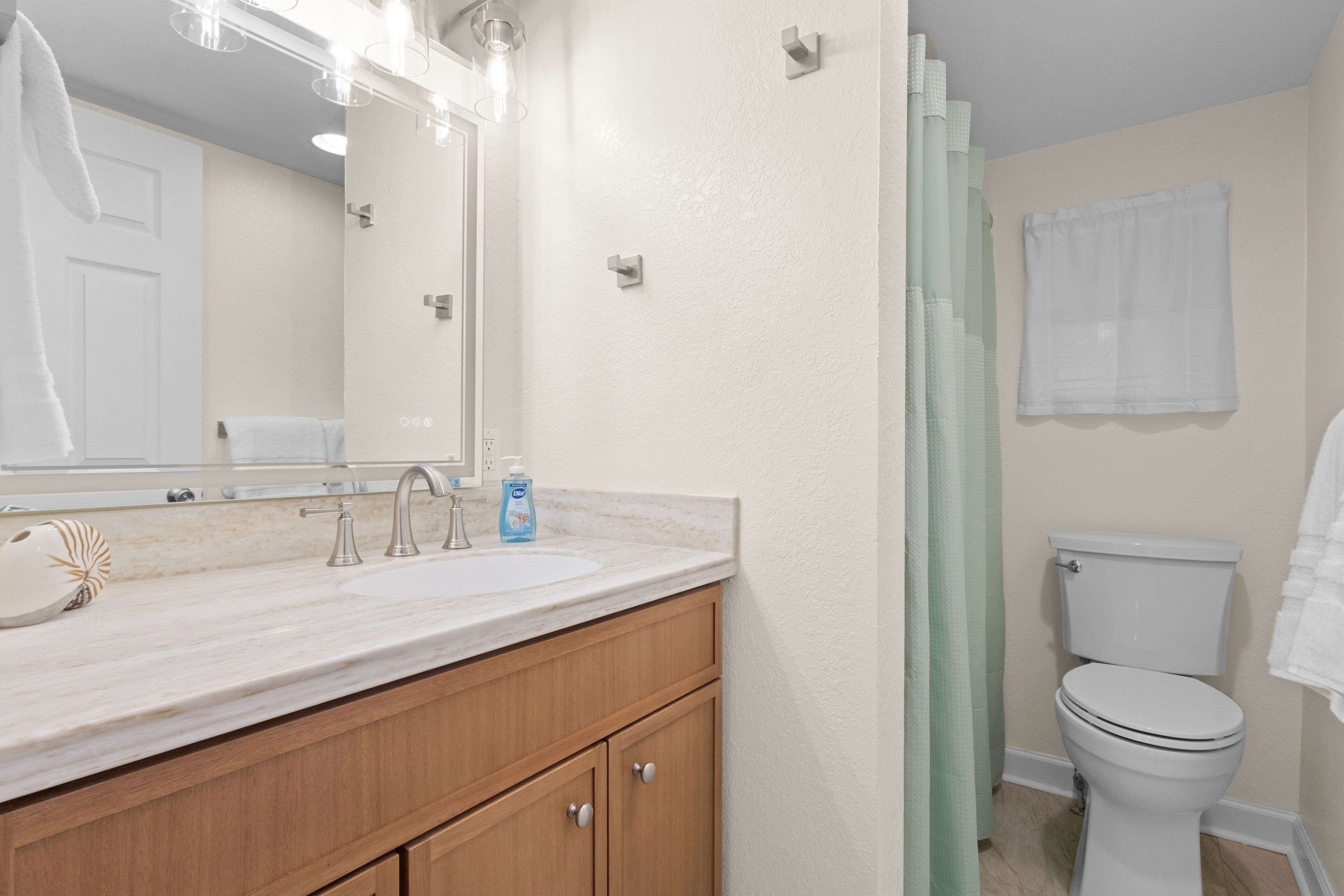 A bathroom with a white sink, wooden cabinets, a mirror, a toilet, and a shower curtain.
