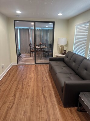 A living room with a sofa, a dining table with chairs, and a sliding glass door leading to a balcony. - Priya’s Island- sleeps 10 with private dock (Steinhatchee)