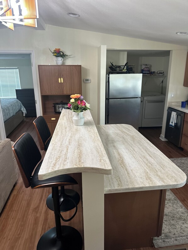 A modern kitchen with a marble countertop, a refrigerator, and a dining area with chairs.
