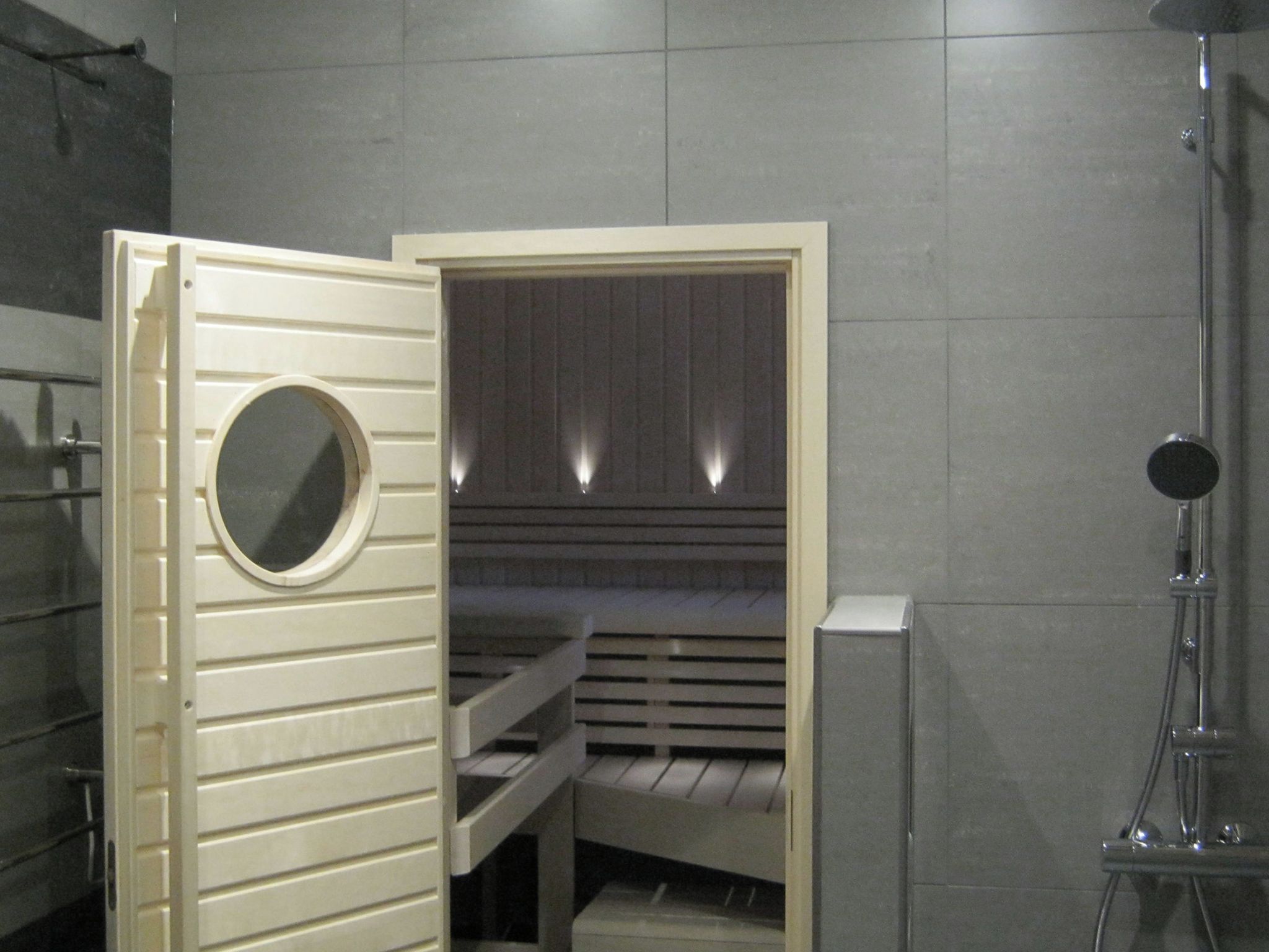 Sauna, jossa on puinen penkki, pyöreä ikkuna ja suihkutila.