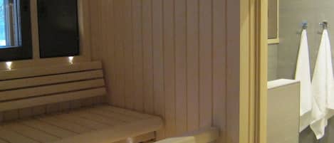 A sauna room with a bench and a glass door leading to a shower area with towels.