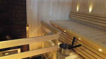 A sauna room with wooden benches and a metal bucket with a black handle.