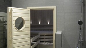 A sauna with a wooden bench, a circular window, and a metal showerhead. - Aaretti by Interhome (Padasjoki)