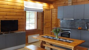 A wooden cabin interior with a dining table, benches, a TV, and a kitchen area. - Aaretti by Interhome (Padasjoki)