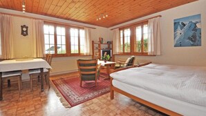 Um quarto aconchegante com teto de madeira, uma cama, uma mesa de jantar com cadeiras e uma estante.