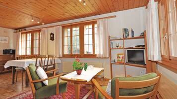 Ein gemütliches Zimmer mit Holzböden, einem Esstisch mit Stühlen, einem Bücherregal und einem Fernseher.