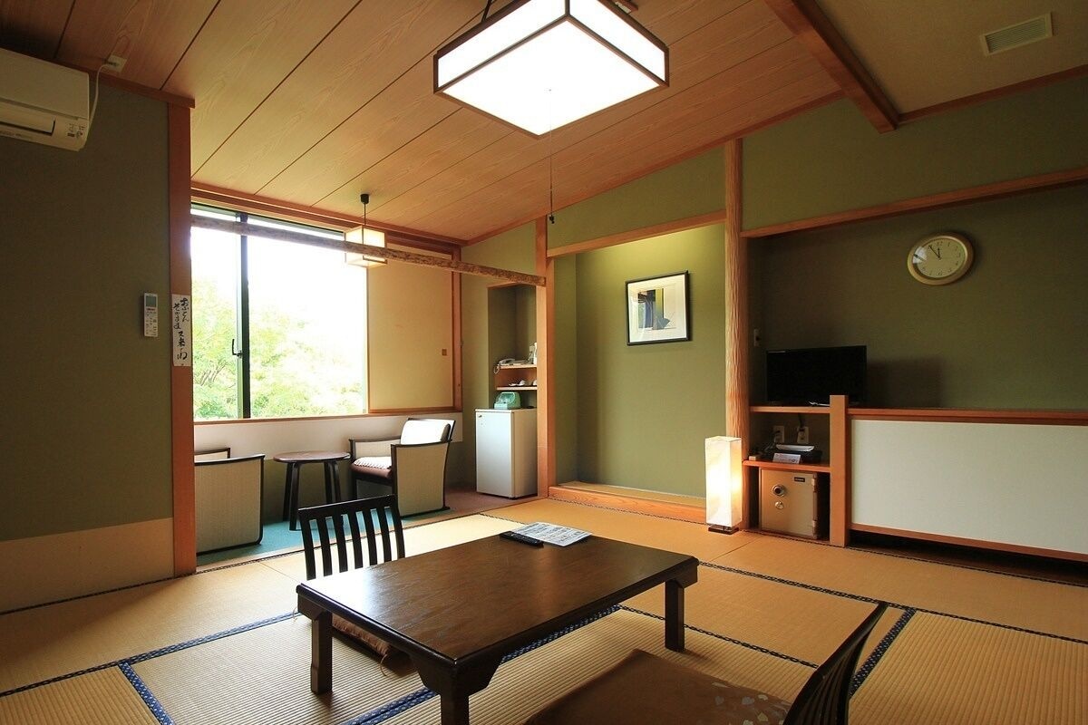 A traditional Japanese room with tatami flooring, a low table, a chair, a small cabinet, and a television.