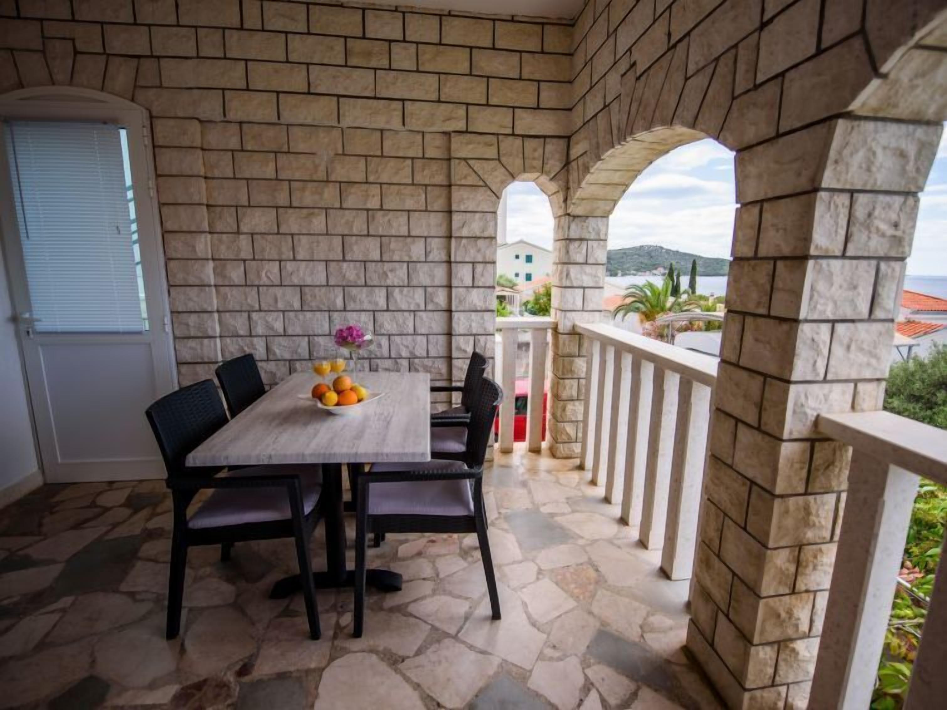 A stone-floored patio with a table set for two, featuring a fruit bowl and a vase.
