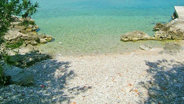 A pebble beach with clear water and rocky outcrops.