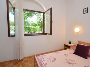 A bedroom with a bed, a nightstand, a lamp, and a window with curtains. - Apartment Rose by Interhome (Brodarica/Žaboric)