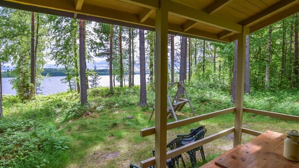 En träveranda med ett bord och stolar, med utsikt över ett skogsområde och en sjö.