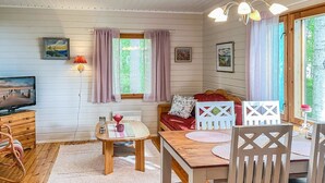 En mysig stuga med en matplats inredd med ett träbord, stolar, en tv och en soffa.
