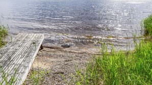 En träbrygga som sträcker sig ut i en stilla sjö, med en skogbeklädd strandlinje i bakgrunden.