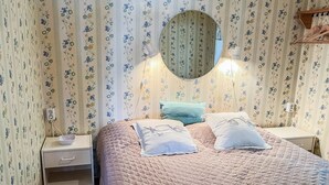 Ett sovrum med blommigt tapetmönster, en rund spegel, en säng med ett quiltat överkast och sängbord med lampor.