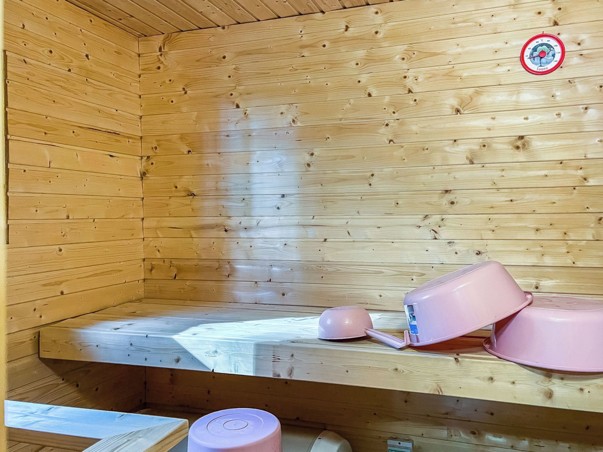 A sauna room with wooden walls, a bench, and a sauna thermometer.