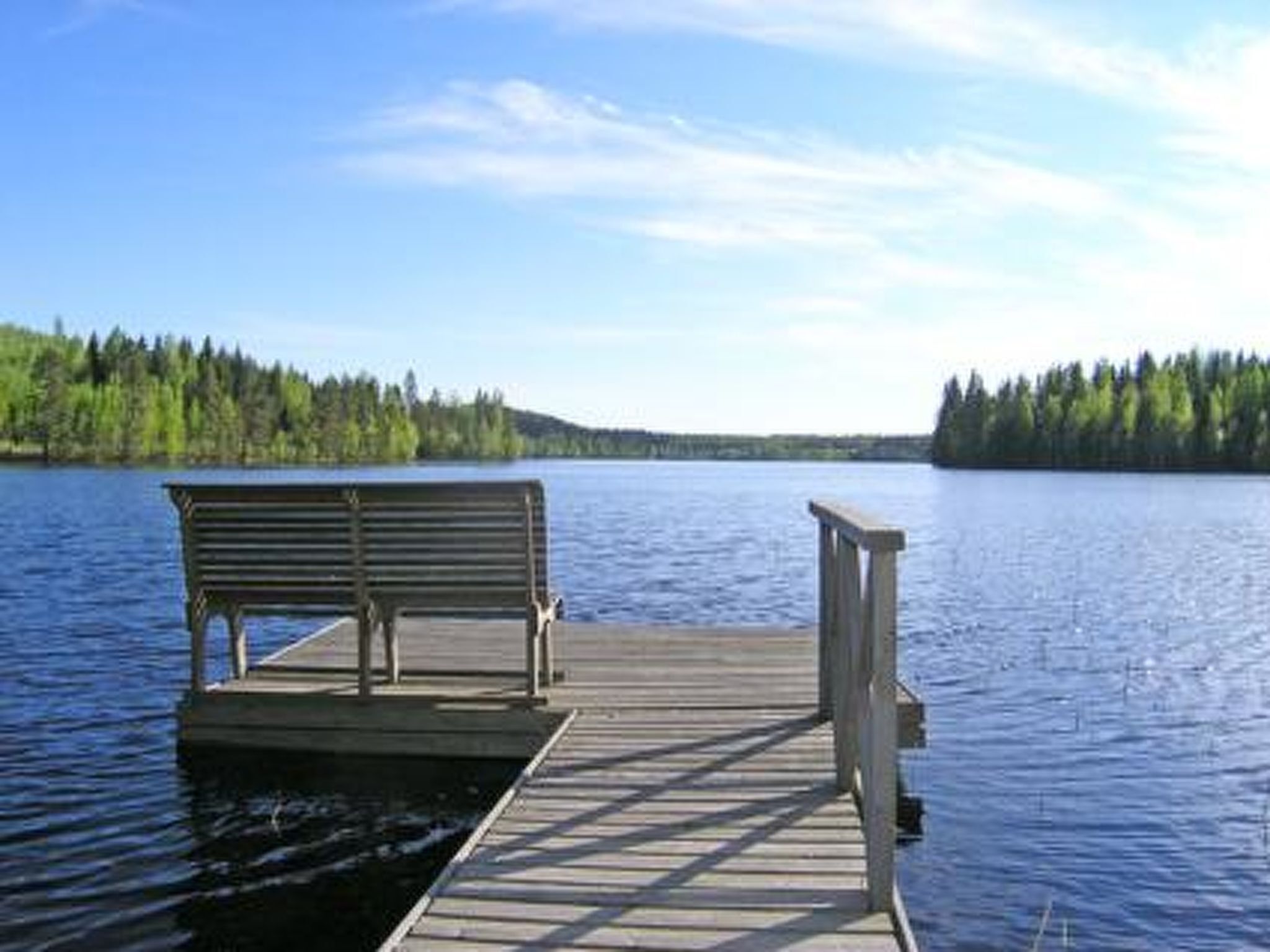 Un molo di legno che si protende in un lago tranquillo, con una panchina all'estremità.