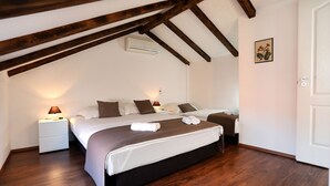 A bedroom with a large bed, wooden beams, a nightstand with a lamp, and a door. - Vila SanAdrija (Trogir)
