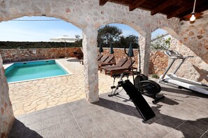 A stone-walled outdoor area with a swimming pool, lounge chairs, and exercise equipment.