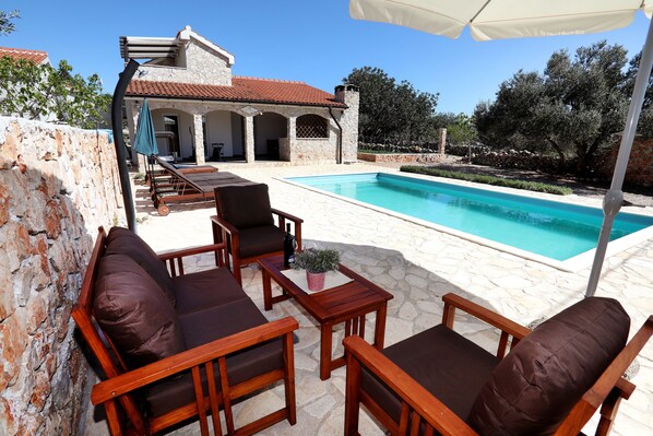 A poolside area with wooden furniture, a stone wall, and a clear view of the pool.