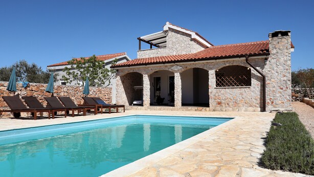 A poolside area with a stone building, lounge chairs, and a clear blue pool. - Vila SanAdrija (Trogir)