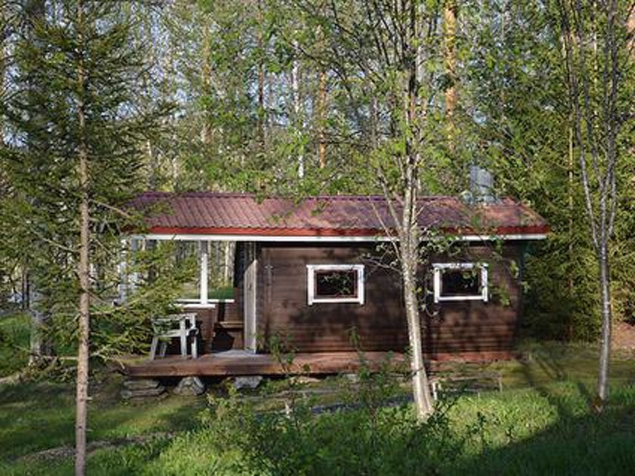 Une cabane rustique avec un toit en métal, entourée d’arbres et d’une zone herbeuse.