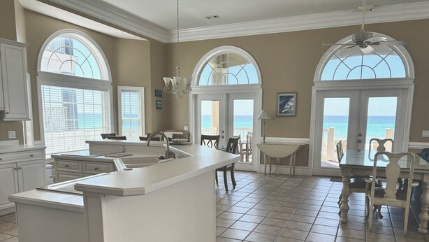 A spacious kitchen with a large island, multiple windows with ocean views, and a dining area with a view of the beach.