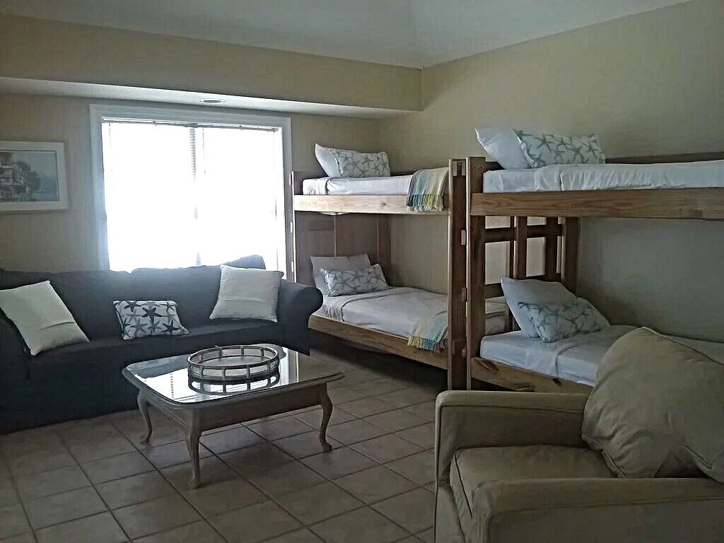 A furnished room with bunk beds, a sofa, a coffee table, and a window providing natural light.