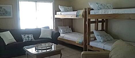 A furnished room with bunk beds, a sofa, a coffee table, and a window providing natural light.