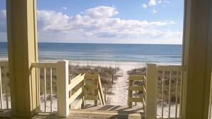 A wooden deck leading to a beach with a clear view of the ocean and sky.
