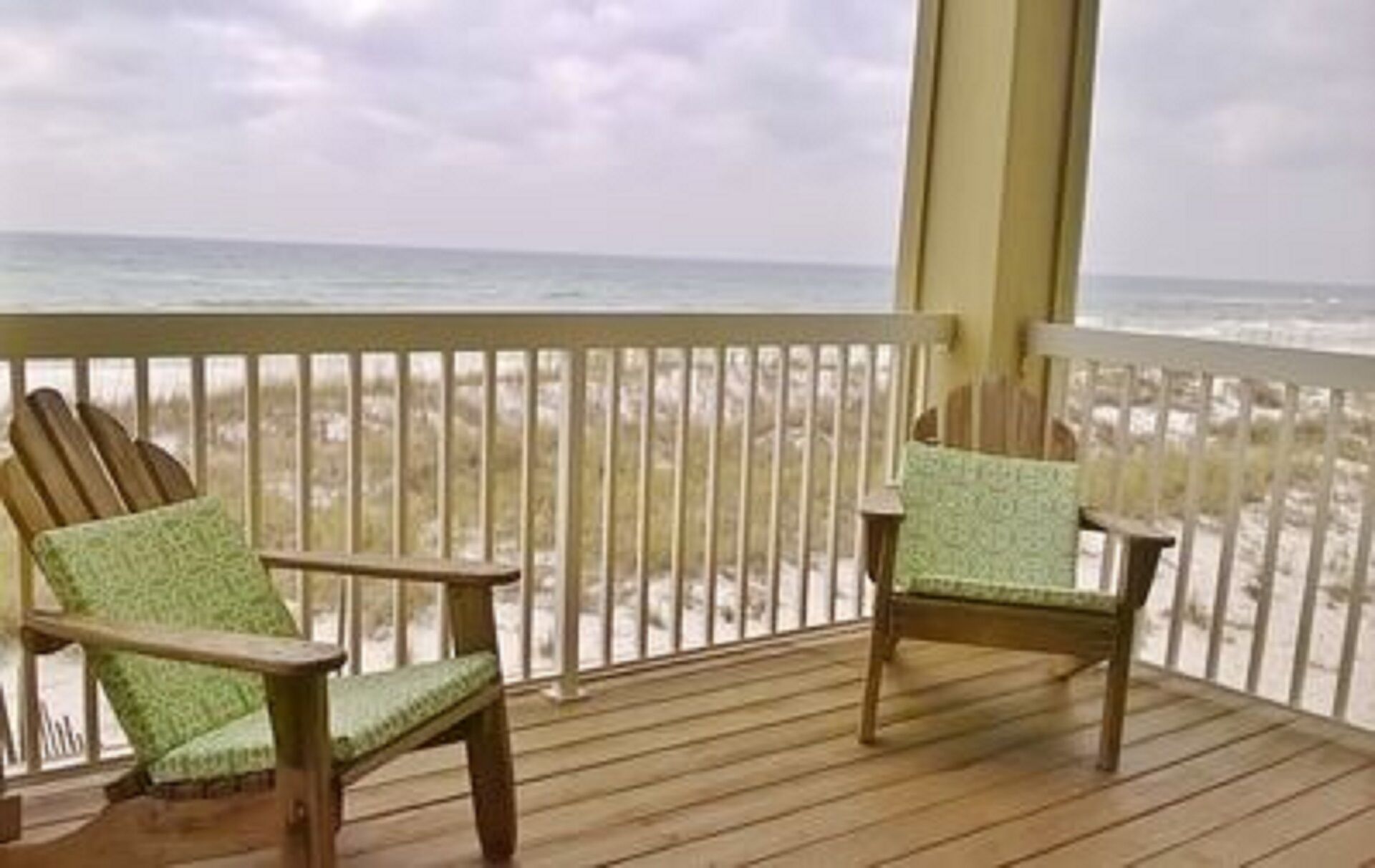 A wooden deck with two Adirondack chairs facing a beach.