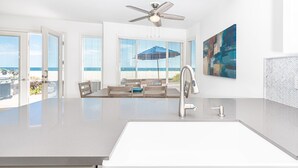 Una cocina moderna con una isla grande, un ventilador de techo y vistas a la playa a través de amplias ventanas.