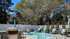 An outdoor patio with a stone fire pit, lounge chairs, and a pool.