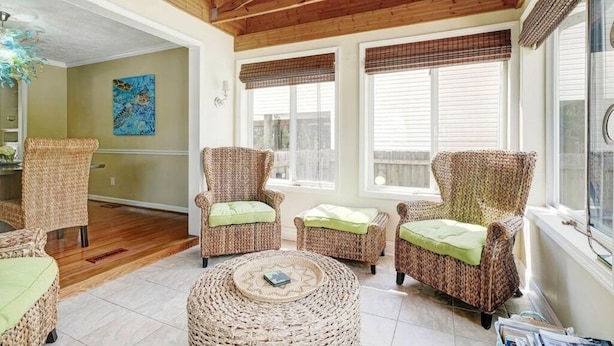 A spacious room with wicker furniture, large windows with blinds, and a ceiling fan.