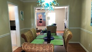 A dining area with wicker chairs, a table with green placemats, and a chandelier.