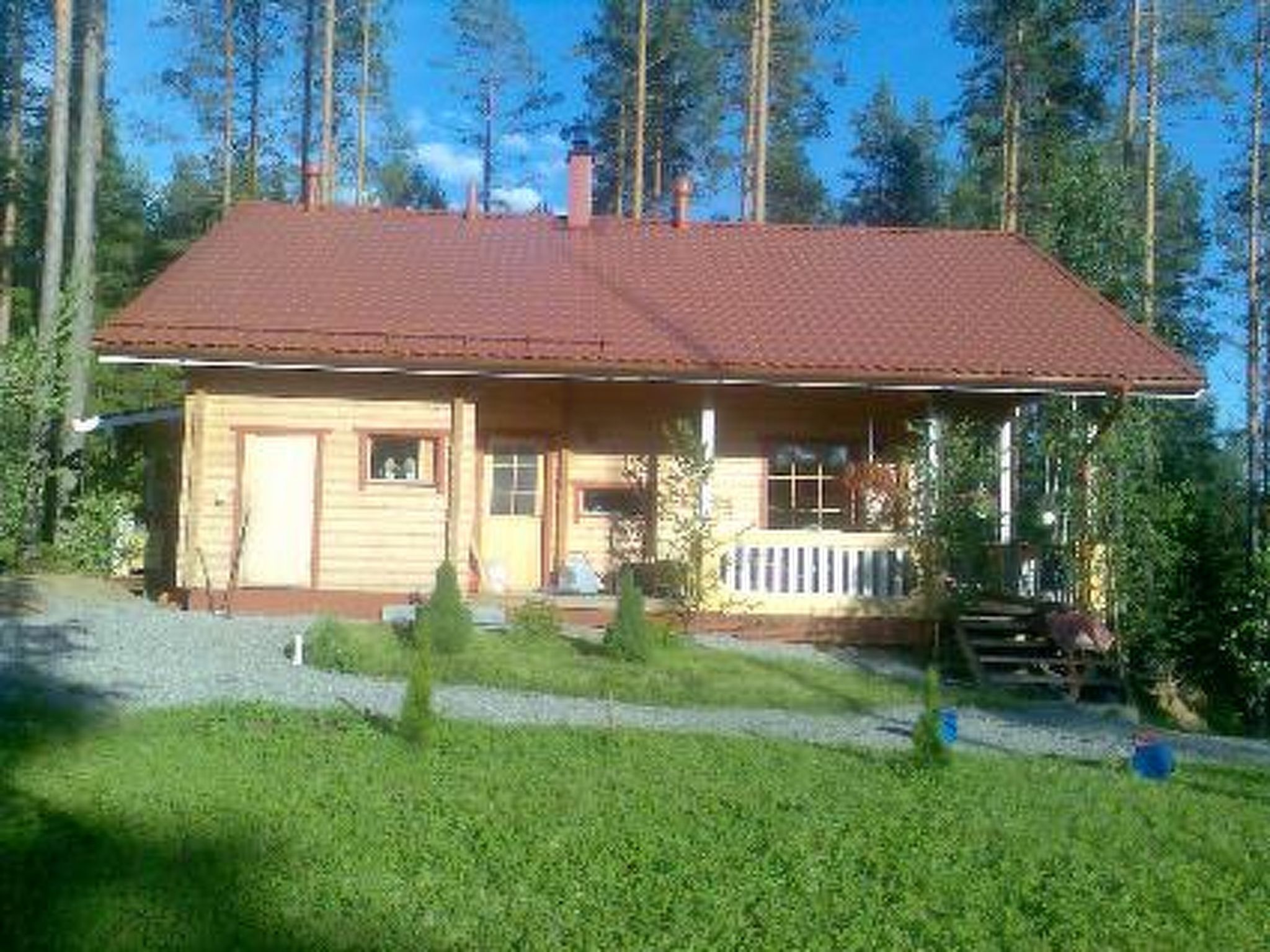 Punatiilikattoinen, puinen mökki, jossa on kuisti ja pieni etupiha.