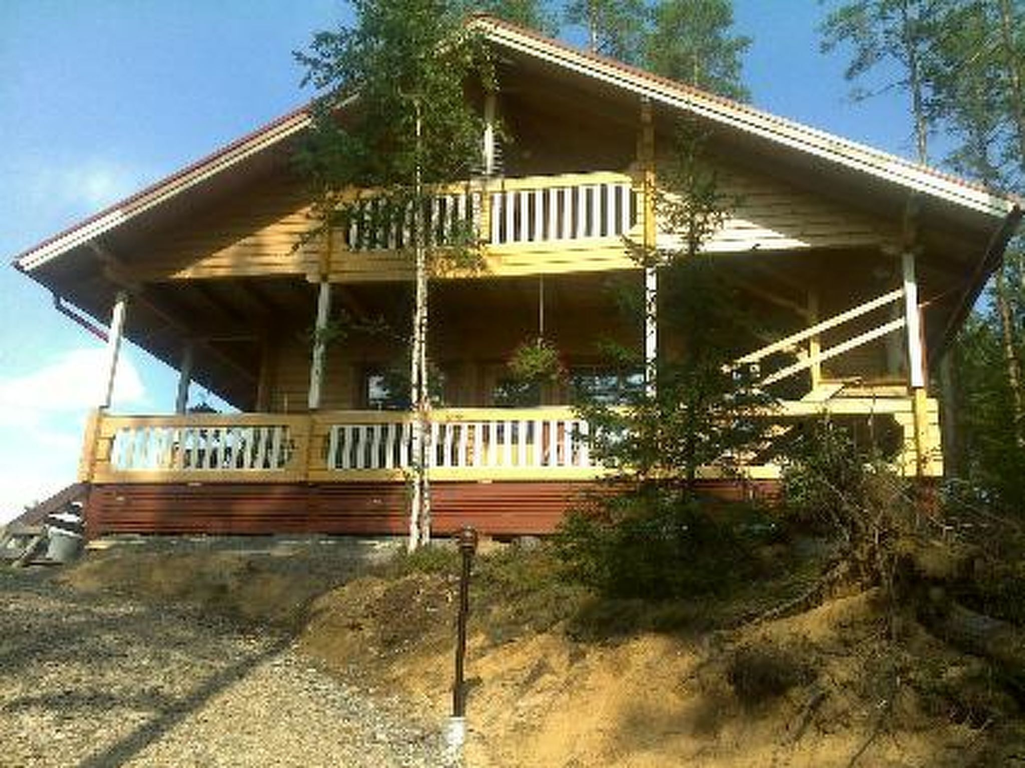 A two-story wooden house with a porch, surrounded by trees and a hillside.