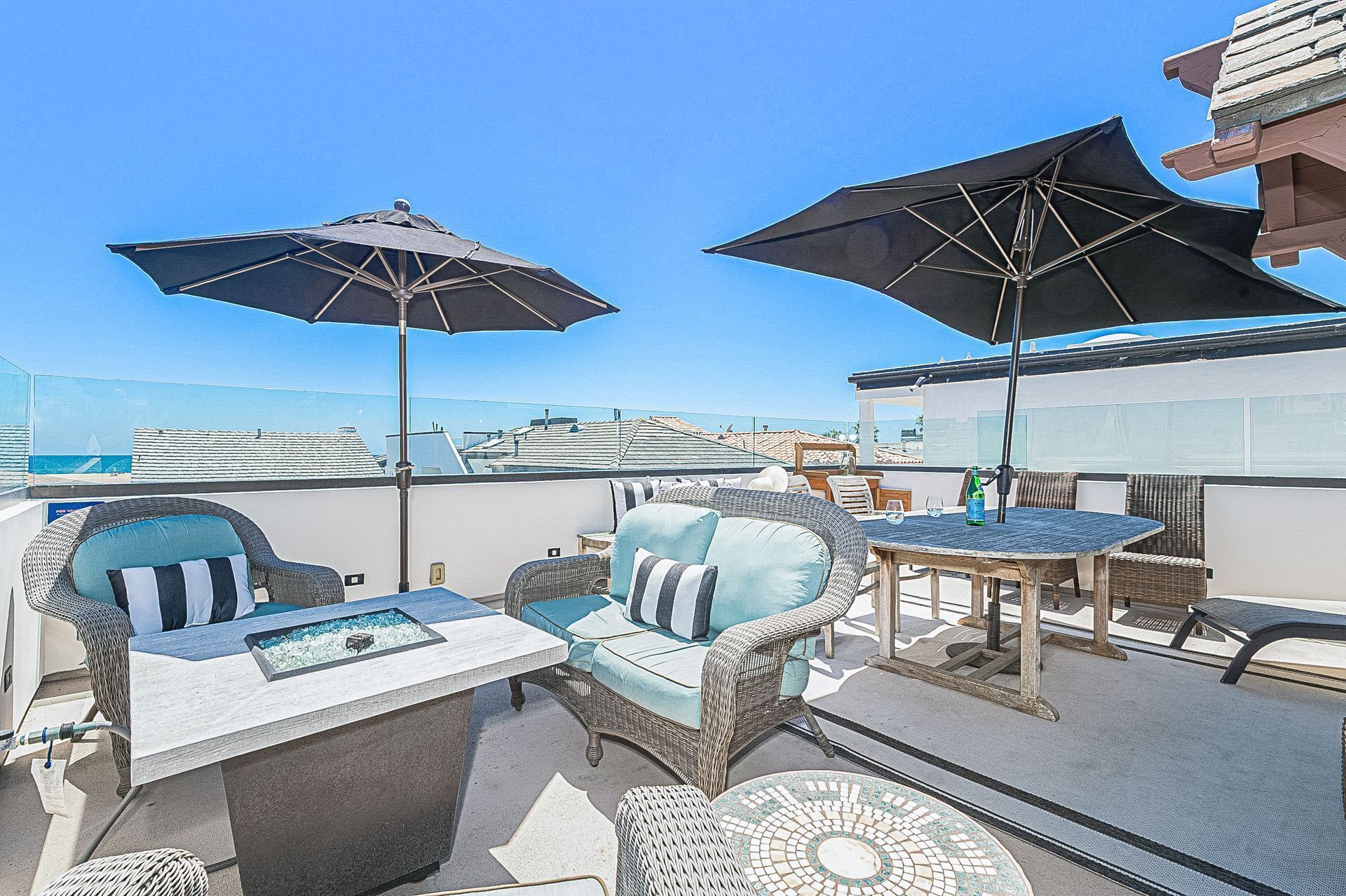 A rooftop terrace with wicker furniture, two large umbrellas, and a view of the sea.