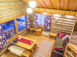 Interior acogedor de una cabaña, con paredes de madera, una mesa de comedor, un sofá y una ventana con cortinas.