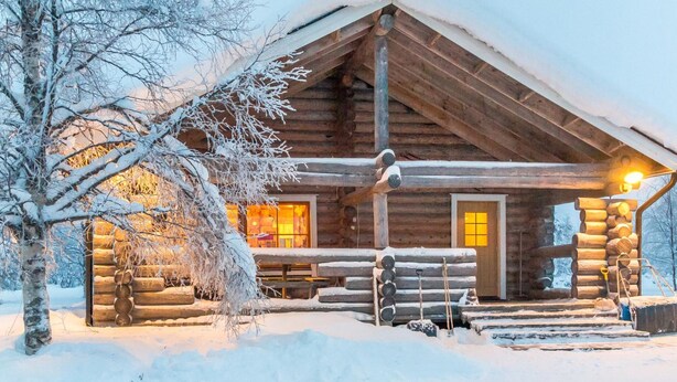 Una cabaña de troncos con un interior acogedor, rodeada de árboles cubiertos de nieve.