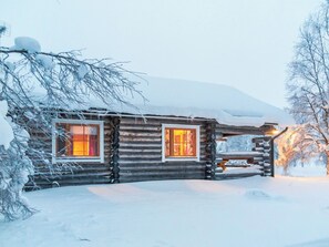 Une cabane en rondins avec deux fenêtres, entourée de neige.