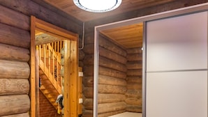 Un dormitorio tipo cabaña de madera con una escalera de madera, una cama, un pequeño cofre de madera y una puerta corredera.