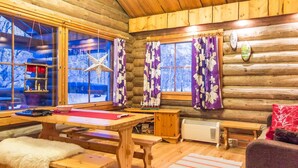 Un acogedor interior de cabaña de madera con muebles de madera, chimenea y ventanas grandes con cortinas.