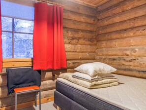 Una habitación tipo cabaña de troncos con una cama, un sillón y una ventana con cortinas rojas.