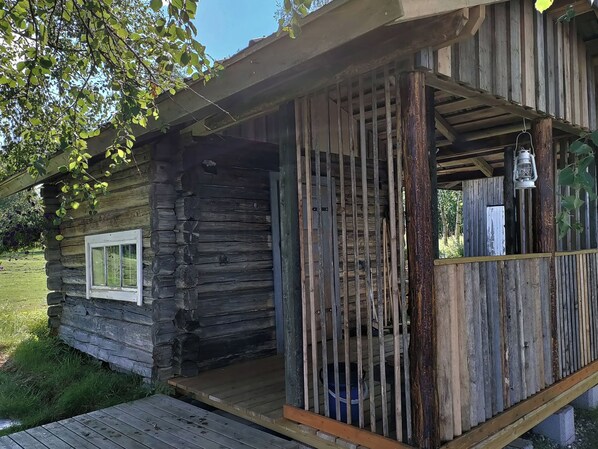 Una cabaña rústica con un porche de madera y una ventana pequeña.