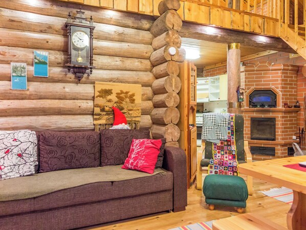 L’intérieur d’une cabane en rondins, avec un mur en bois, une table à manger en bois, un canapé avec des coussins, une cheminée et une horloge.
