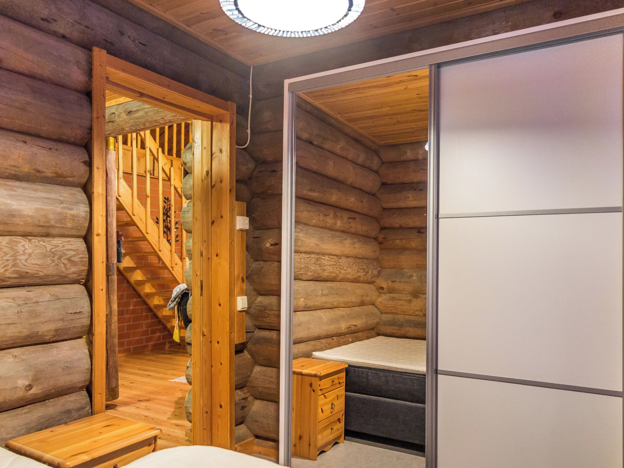 L’intérieur d’une cabane en rondins, avec un escalier en bois menant à une mezzanine, un lit et une armoire.