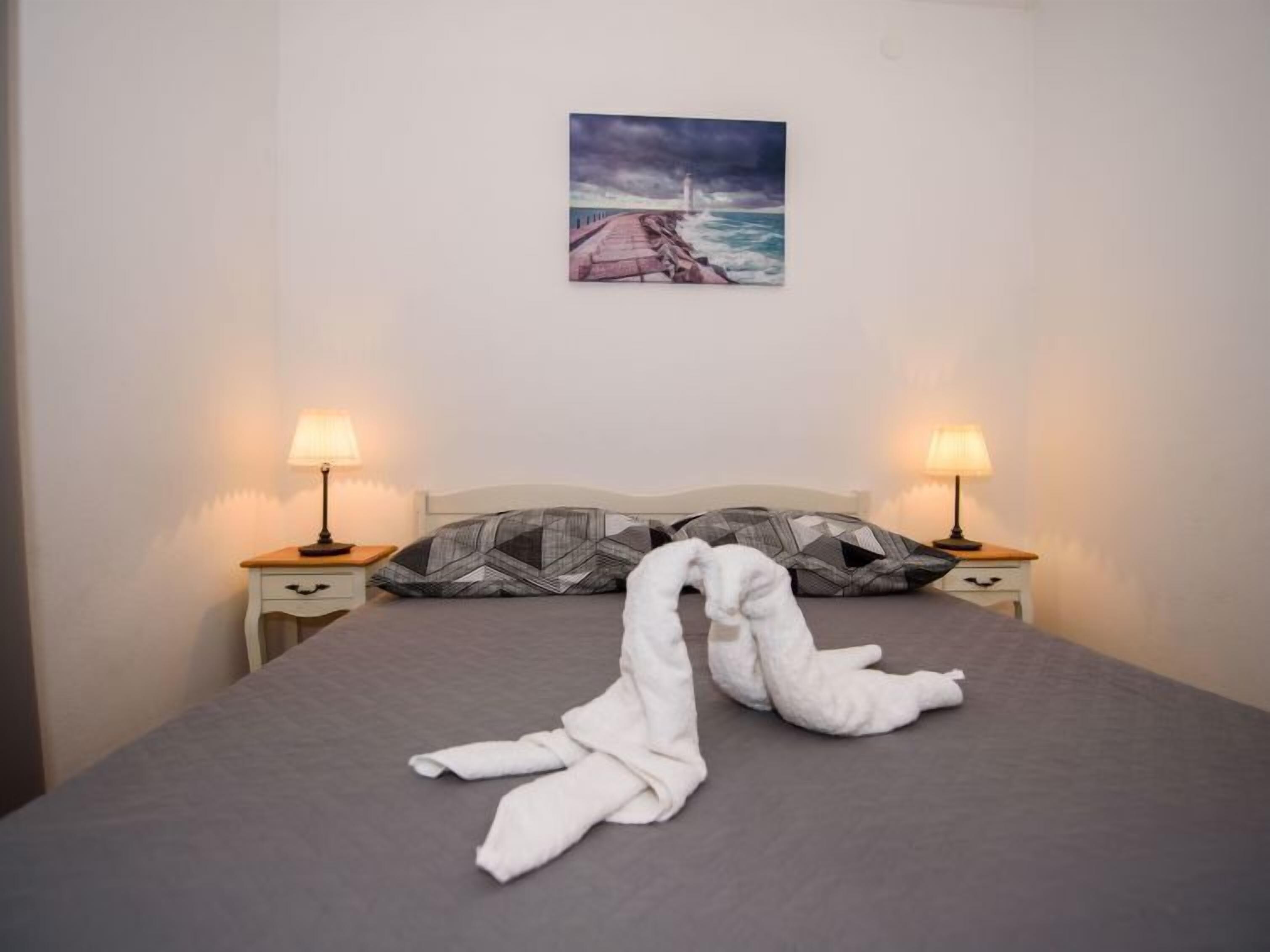 Ein Hotelzimmer mit einem Bett, zwei Nachttischlampen, einem Kopfkissen und einem Gemälde eines Leuchtturms an der Wand.