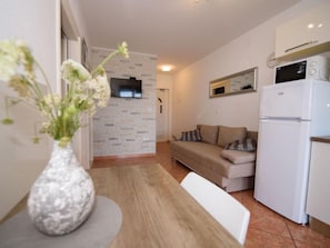 A compact living space with a sofa, a dining table with a vase of flowers, a refrigerator, and a microwave. - Apartment Marina by Interhome (Rogoznica/Ražanj)