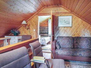 Ein gemütliches Cabin-Interieur mit Holzbalkendecke, einer Couch, einem Esstisch mit Stühlen und einem Bett mit gemustertem Überwurf.